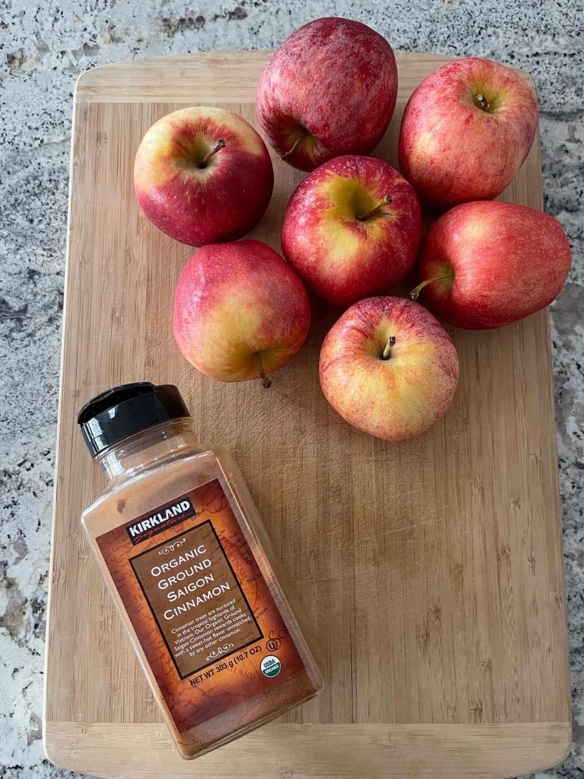 Fresh apples and container of organic ground cinnamon on bamboo cutting board.