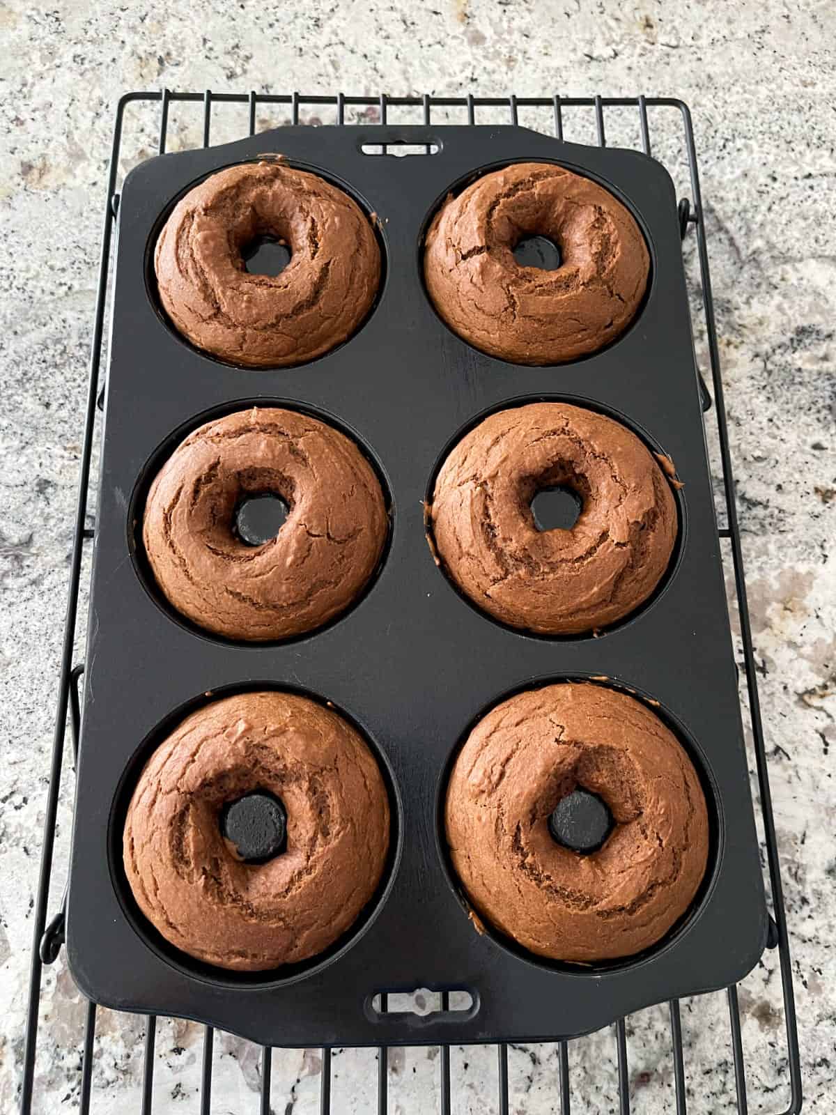 Fresh baked pumpkin spice latte donuts in pan on wire rack.