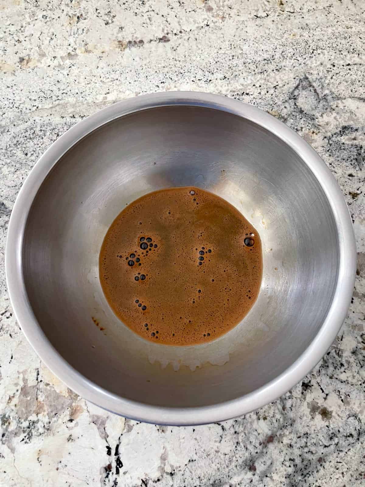 Dissolving instant espresso powder in hot water in mixing bowl.
