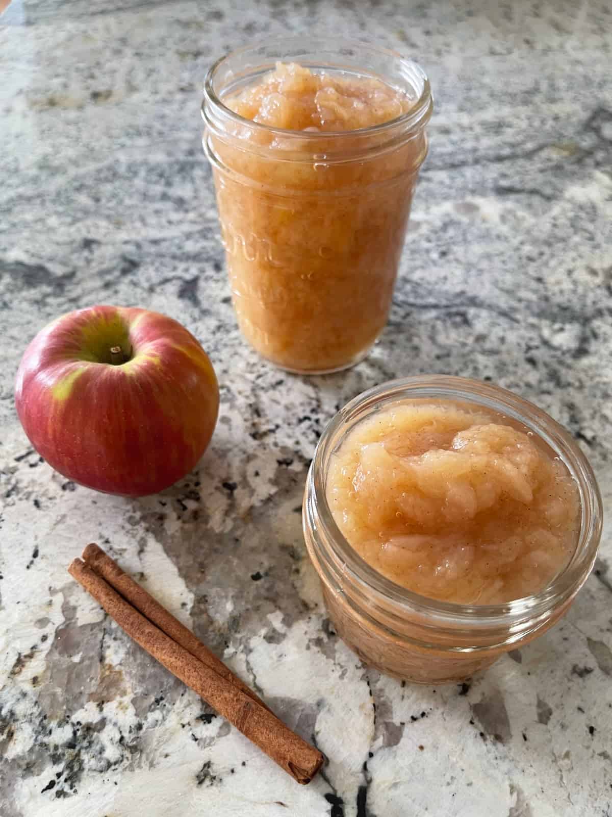 Cinnamon applesauce in two small mason jars near whole fresh apple and cinnamon stick.