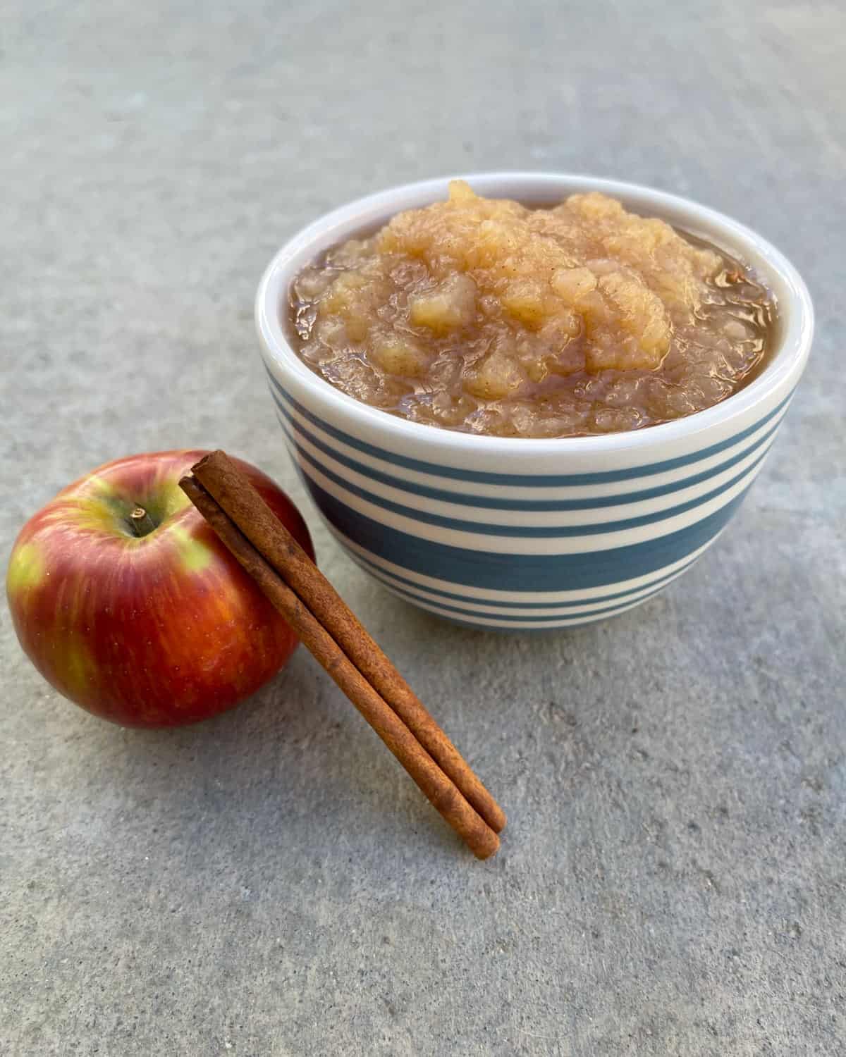 Instant Pot cinnamon applesauce in small bowl near fresh apple and cinnamon stick.