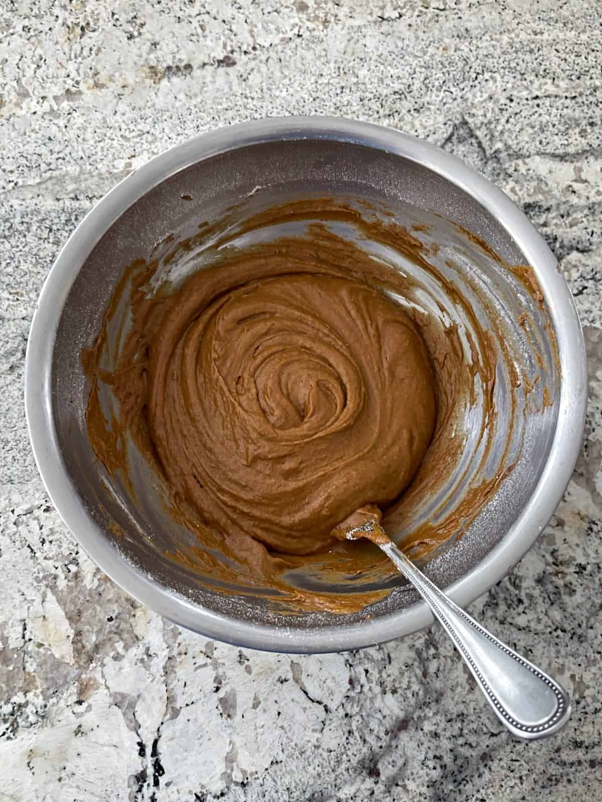 Mixing pumpkin spice latter donut batter in mixing bowl with fork.