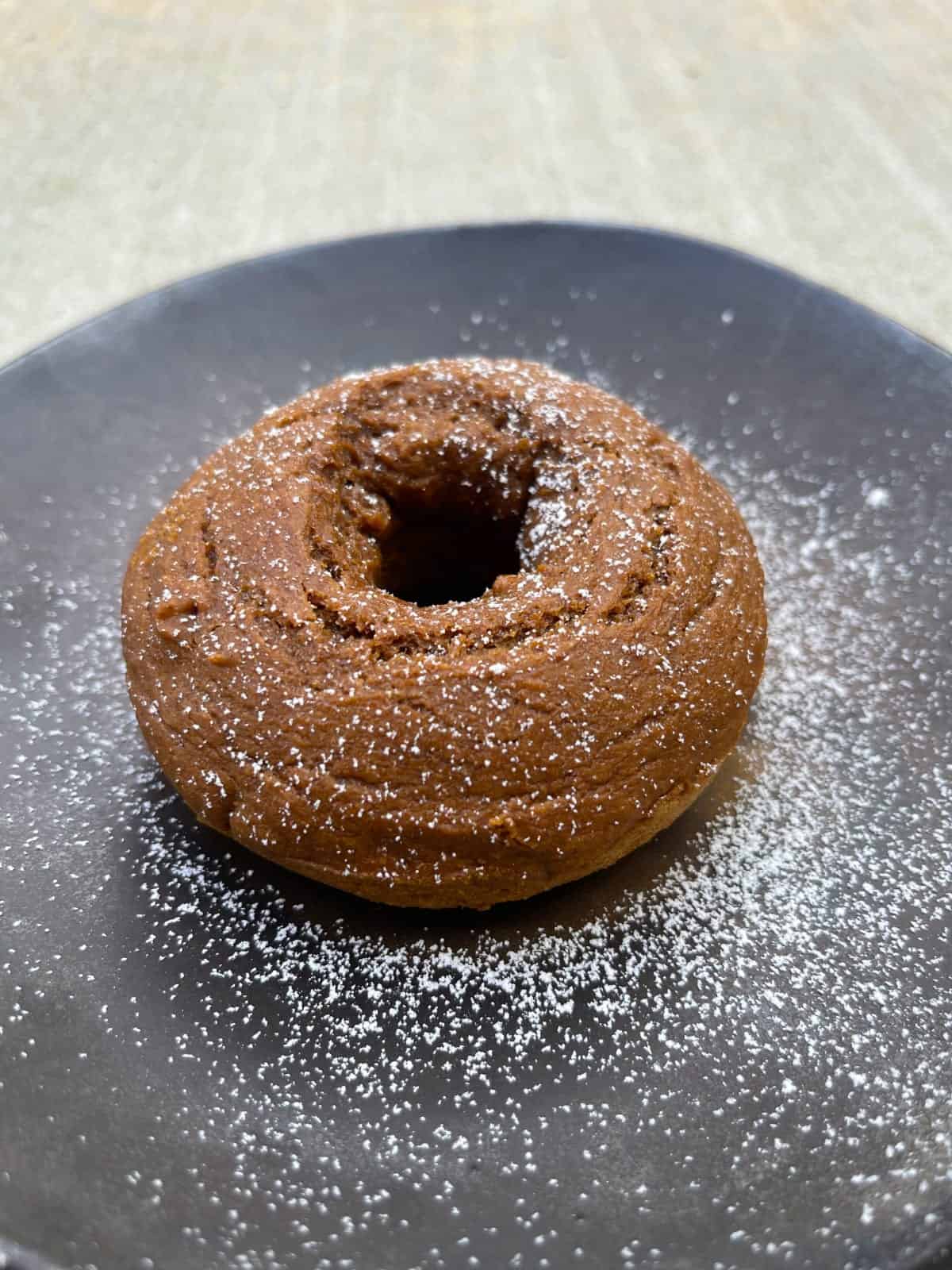 Pumpkin spice latte donut sprinkled with powdered sugar on dark brown plate.