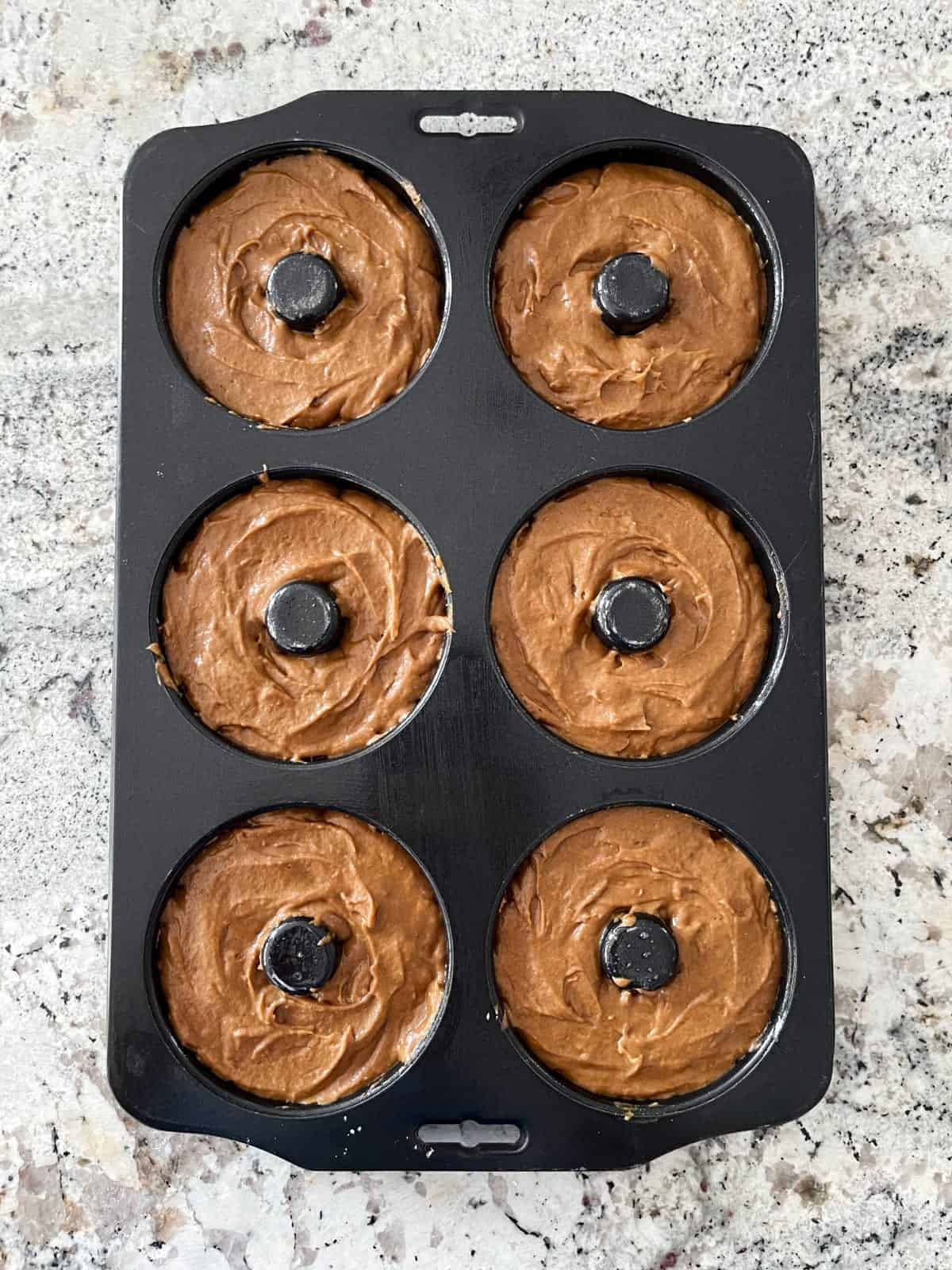 Unbaked pumpkin spice latte donuts in pan on granite counter.