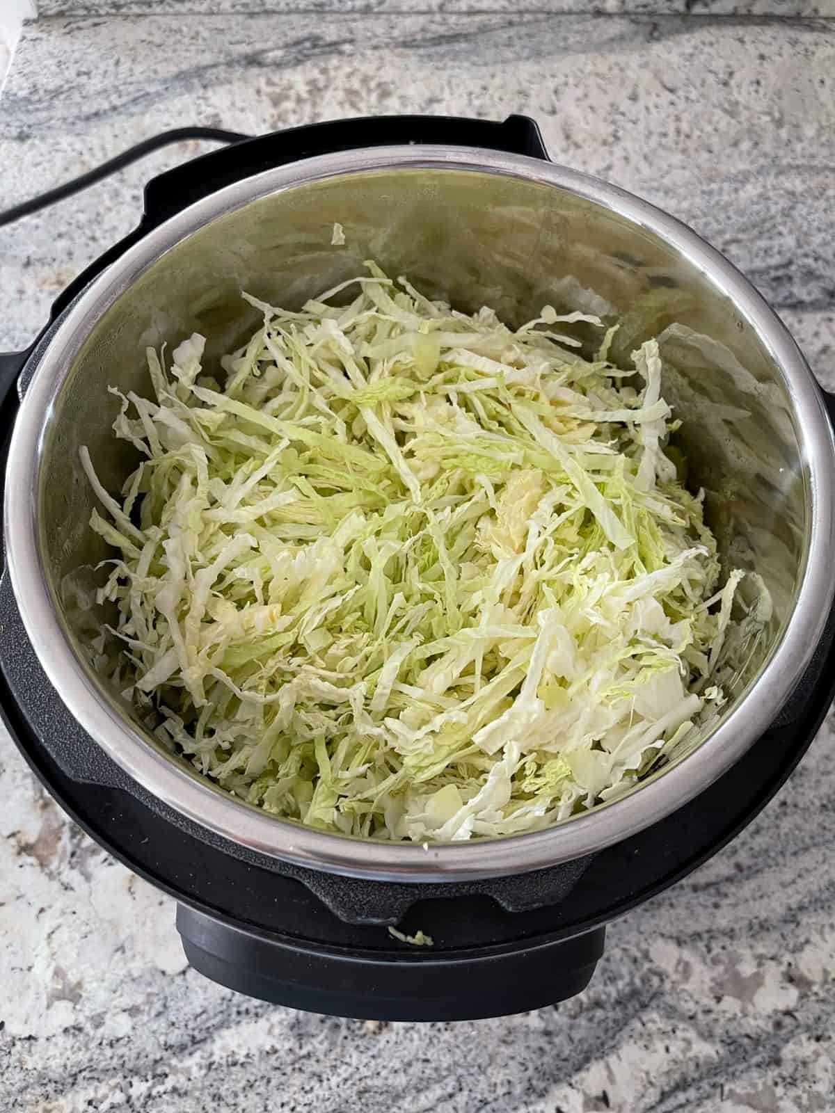 Layering shredded cabbage in Instant Pot for making egg roll bowls.