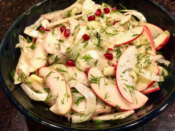 Sliced apple and fennel salad with pomegranate seeds and dill in ceramic bowl