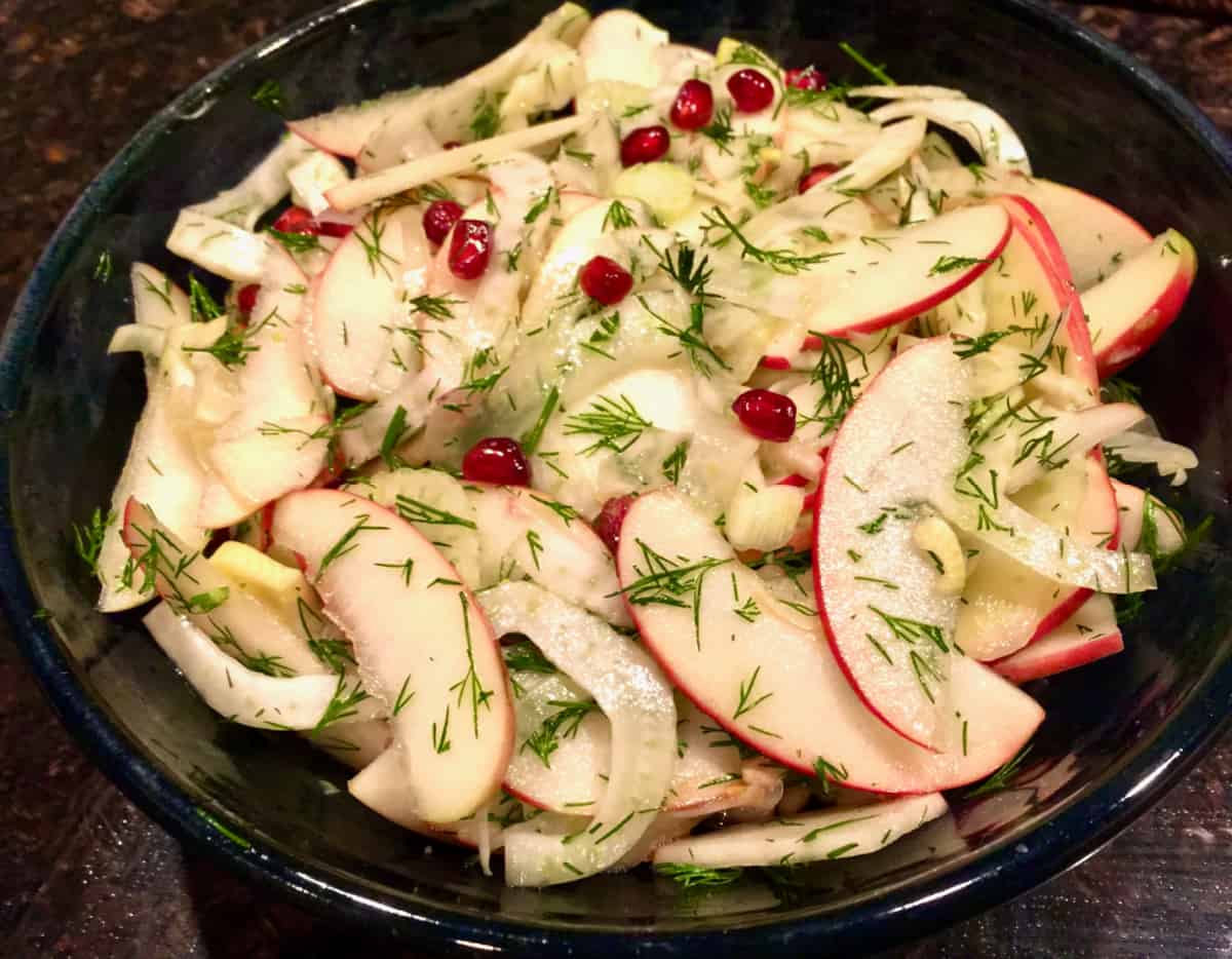 Sliced apple and fennel salad with pomegranate seeds and dill in ceramic bowl.