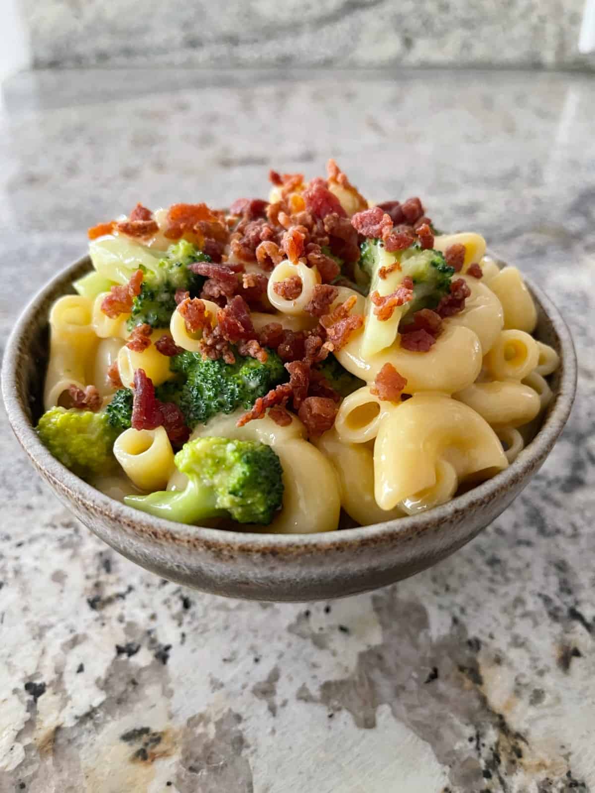 Broccoli bacon macaroni cheese in small brown bowl.