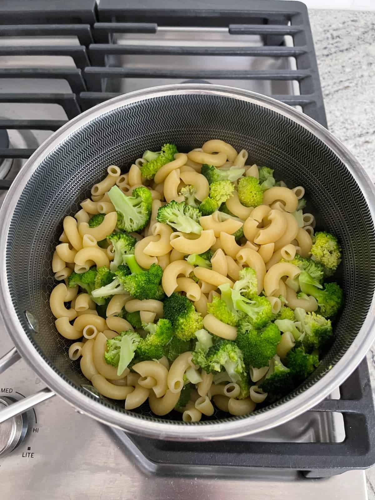 Fresh cooked macaroni and broccoli florets in saucepan.