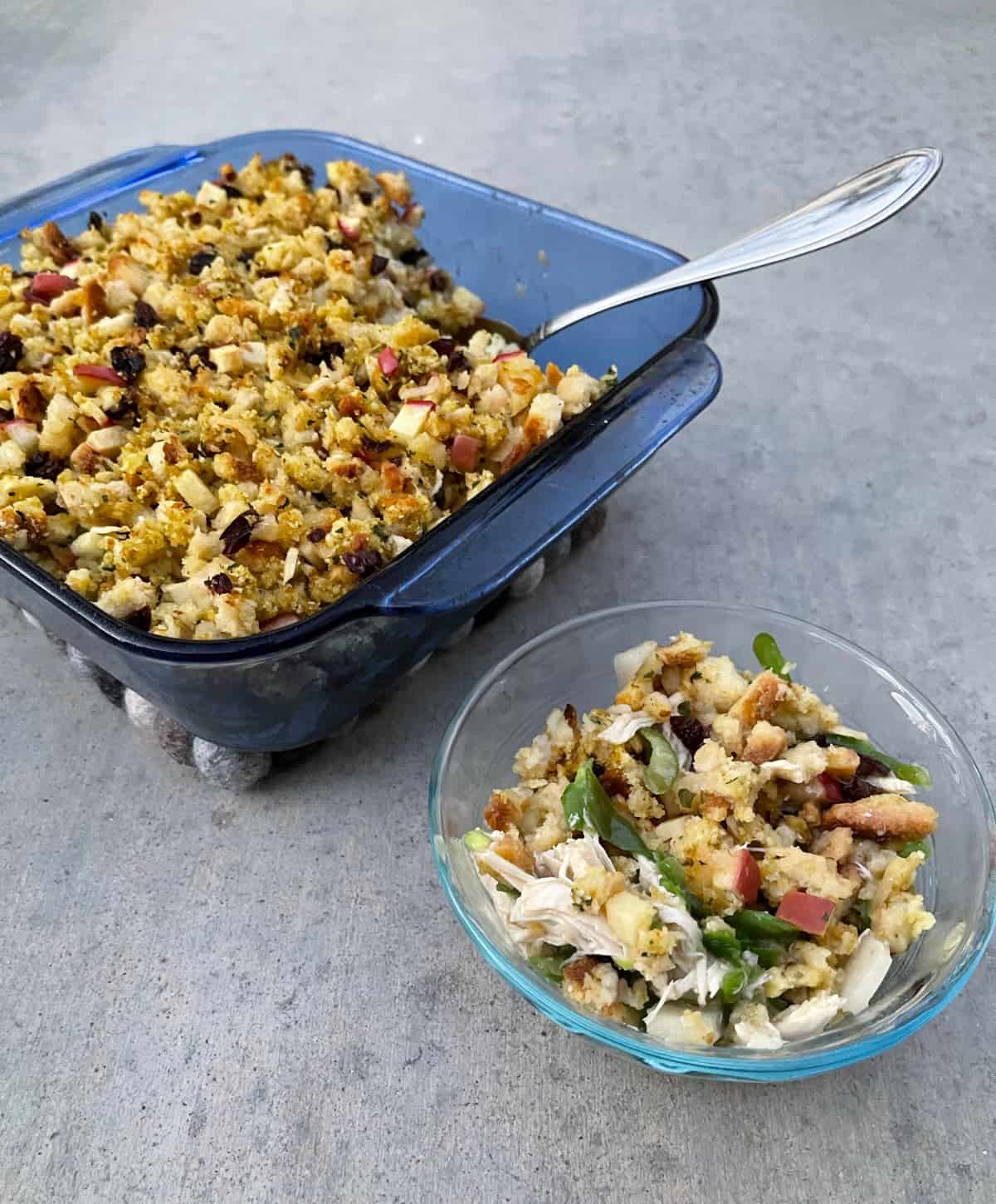 Chicken apple stuffing casserole in baking dish with spoon near small serving in glass bowl.