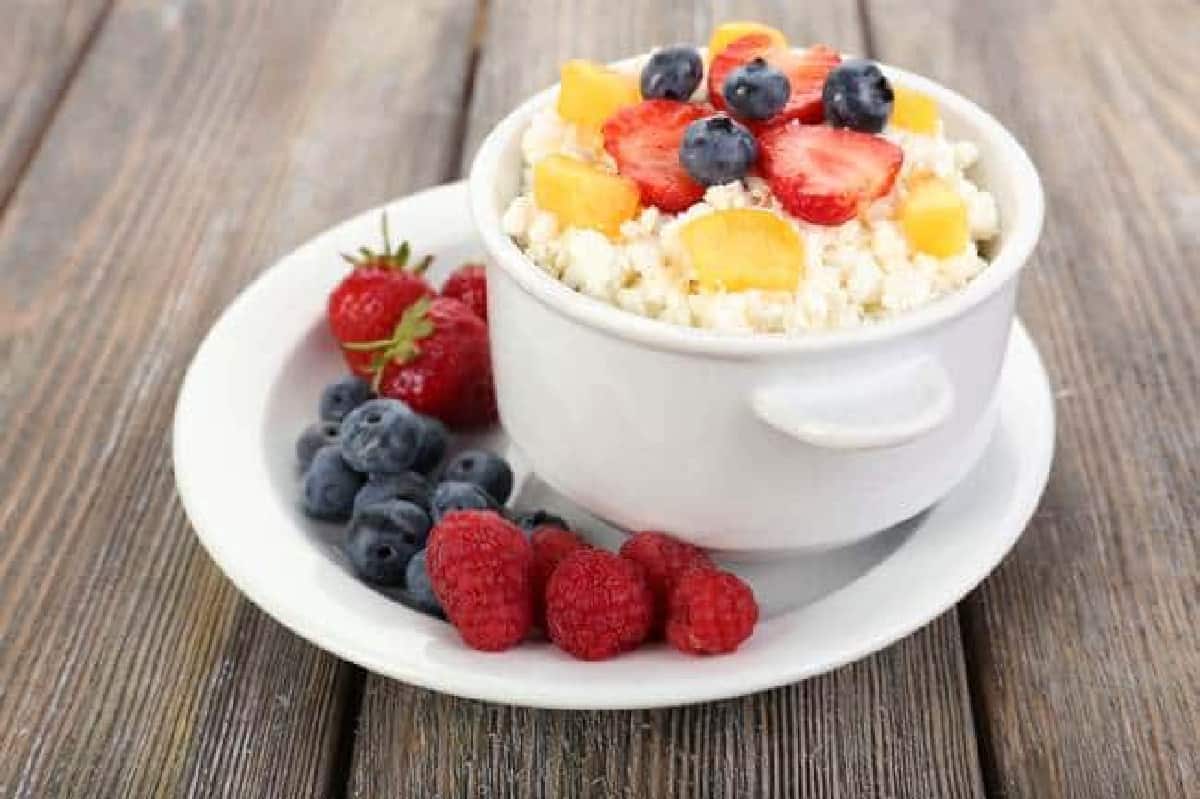 white bowl of cottage cheese topped with fruit and more fruit alongside
