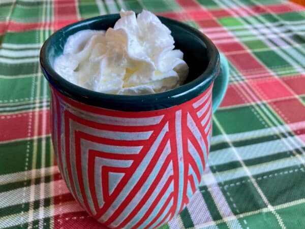 red and green pottery mug with whipped cream topped mocha on holiday plaid tablecloth