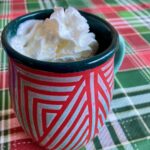 red and green pottery mug with whipped cream topped mocha on holiday plaid tablecloth