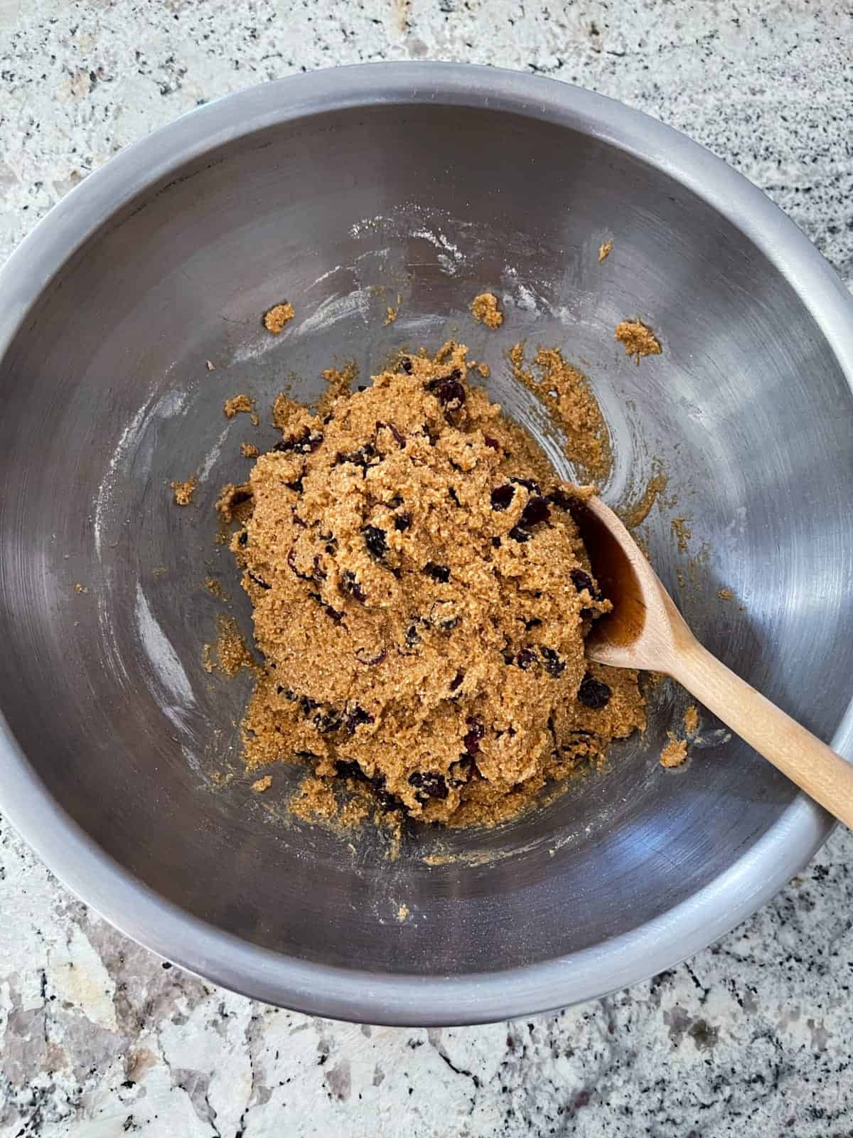Stirring together pumpkin quinoa cookie dough batter with dried cranberries in mixing bowl with wooden spoon.