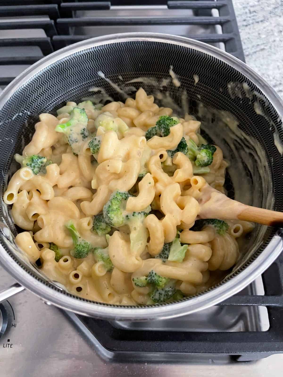Stirring broccoli macaroni and cheese sauce in saucepan.
