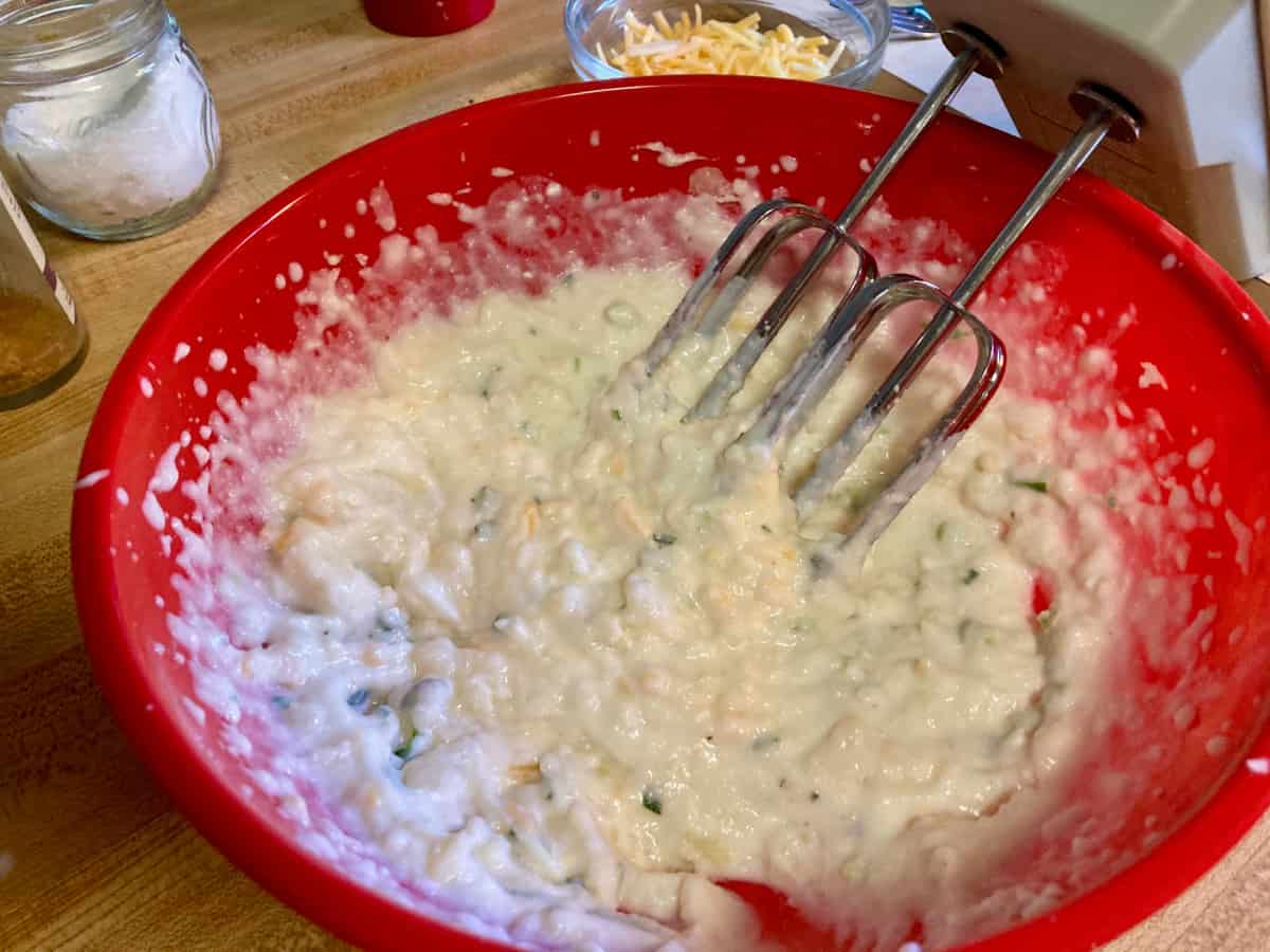 Beating cooked potato, milk, cottage, cheese with electric mixer in red bowl.