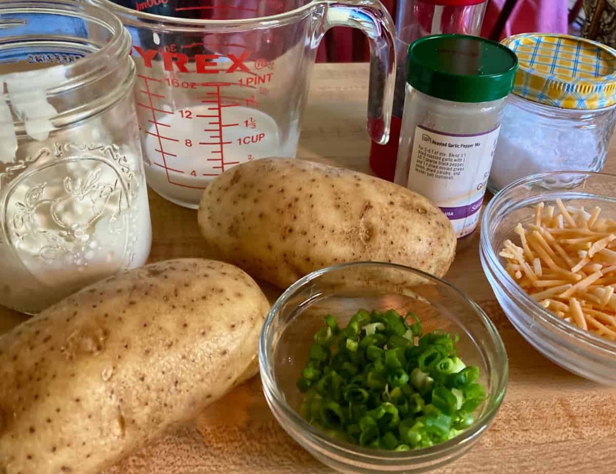 Batatas assadas, cebola verde fatiada, queijo cheddar ralado, leite, requeijão no balcão da cozinha.