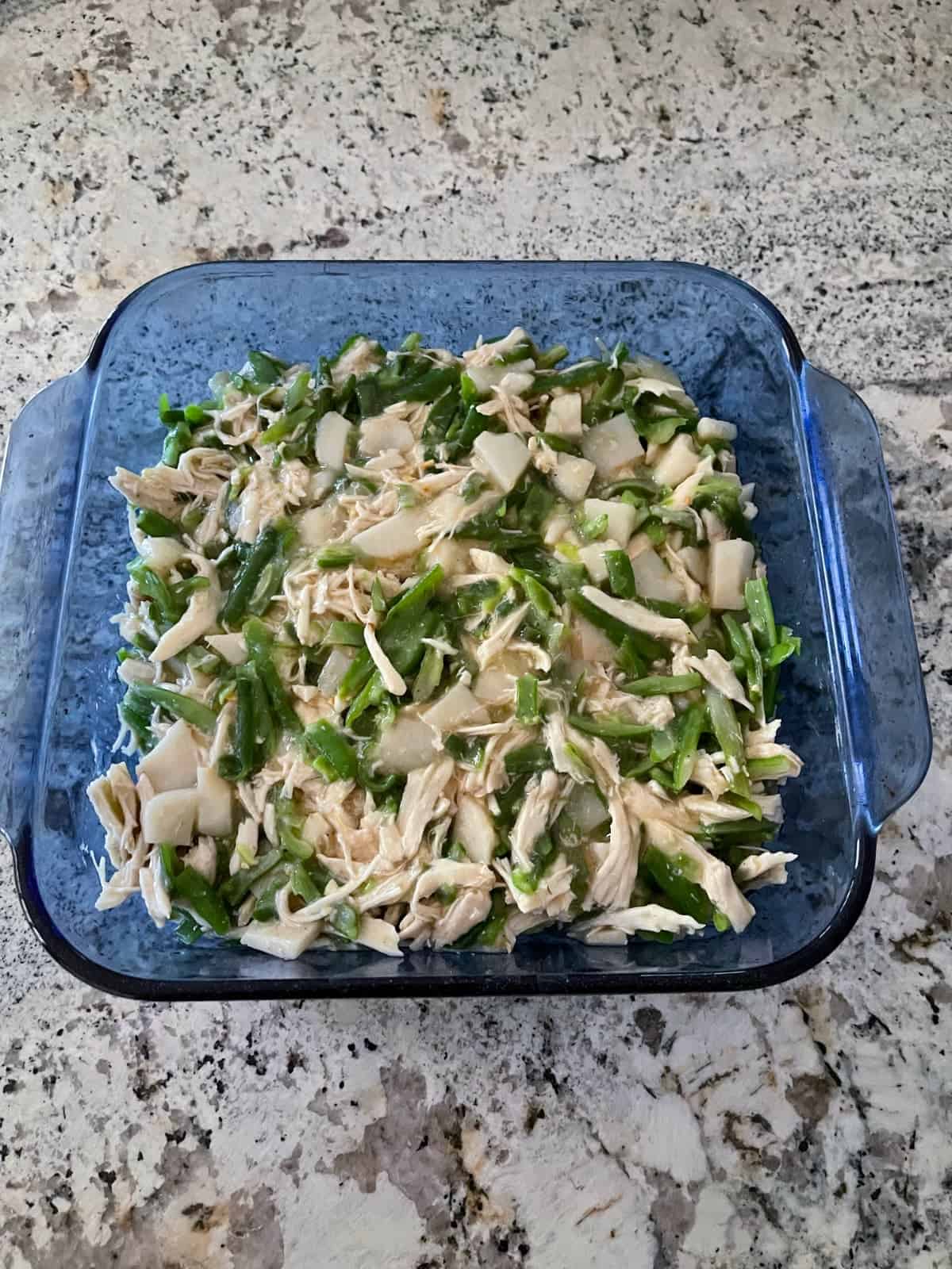 Chicken gravy, green beans, water chestnuts, shredded chicken in square casserole baking dish.