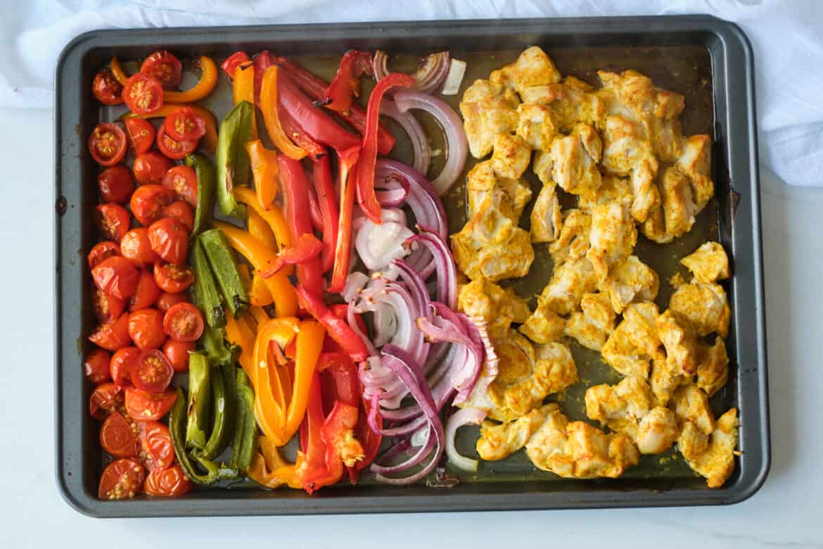 Sheet Pan with rows of tomatoes, bell peppers, red onion and chunks of shawarma chicken.