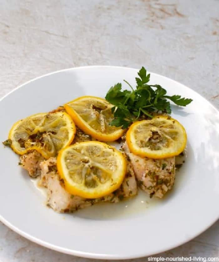 Easy Baked Fish Garnished with Thinly Sliced Lemon on White Plate