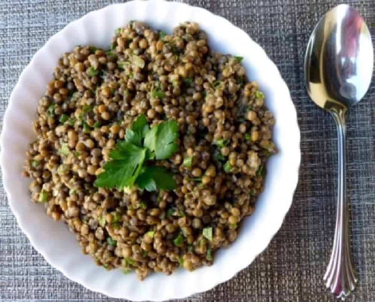 Simple lentil salad garnished with parsley on brown woven tablecloth with spoon alongside.