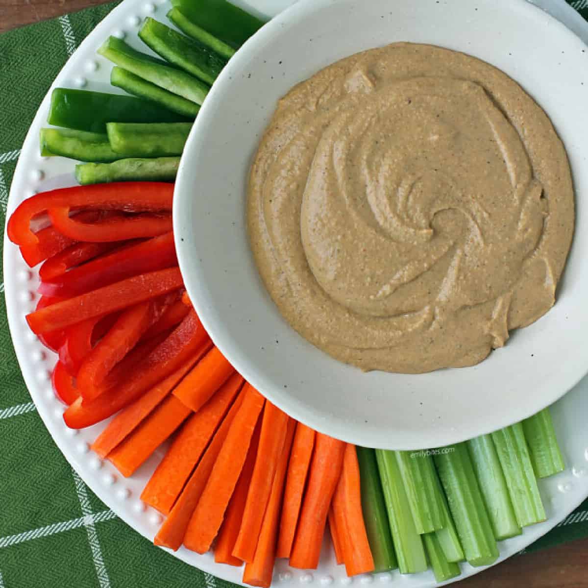 Taco Spiced Hummus in white bowl surrounded by celery and carrot sticks and bell pepper slices