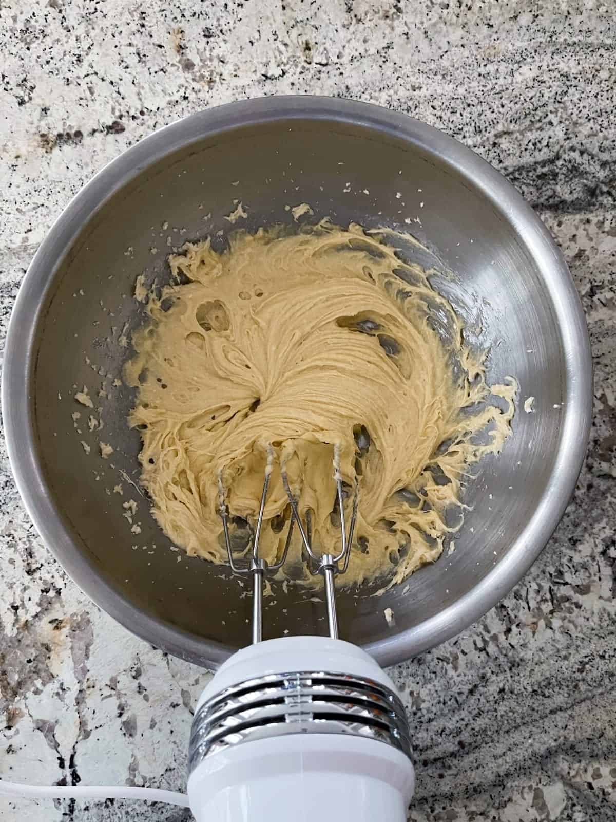 Mixing butter, cream cheese, Truvia, egg yolk, almond extract and orange juice with handheld electric mixer.