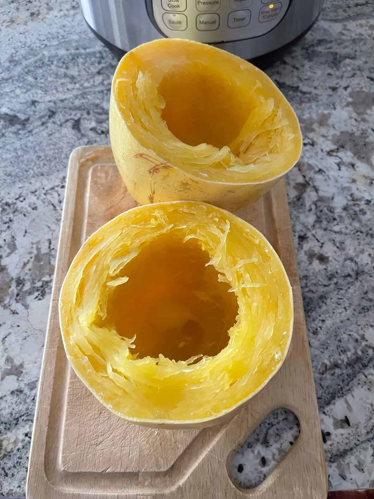 Fresh cooked spaghetti squash halves on wood cutting board with InstantPot in background.