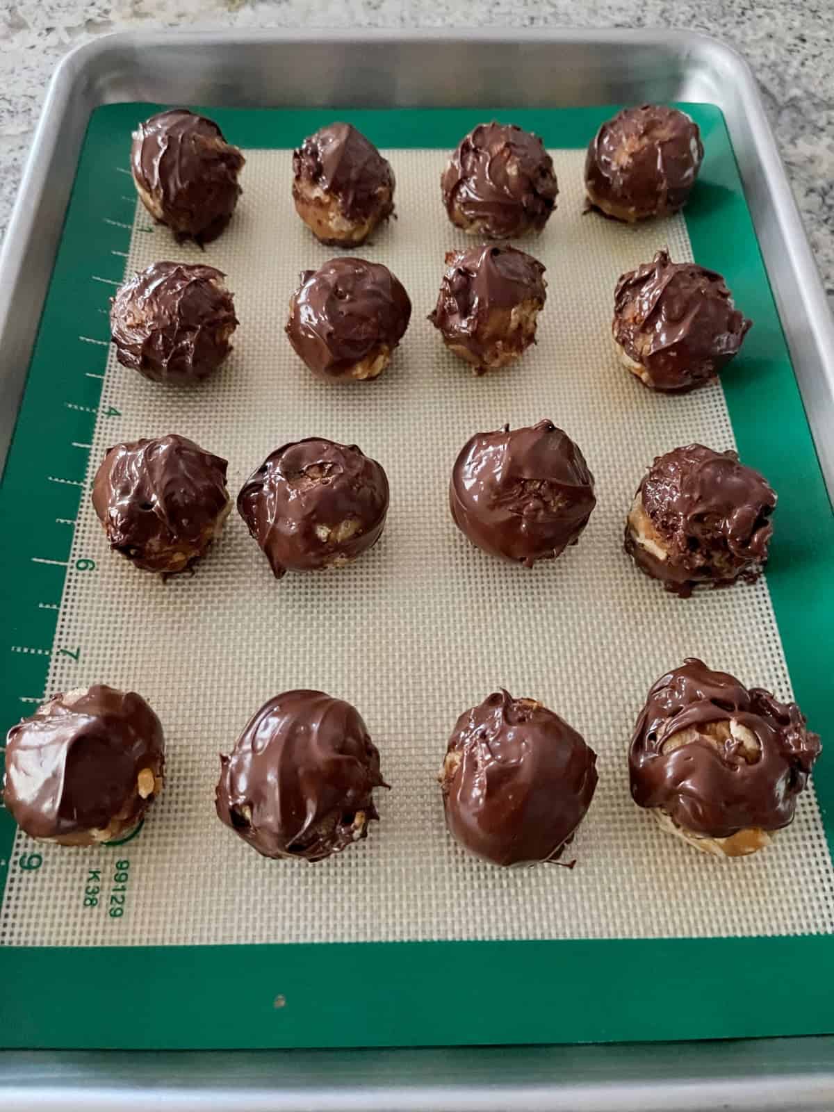 Crispy chocolate peanut butter bon bons on silicone liner on baking sheet.