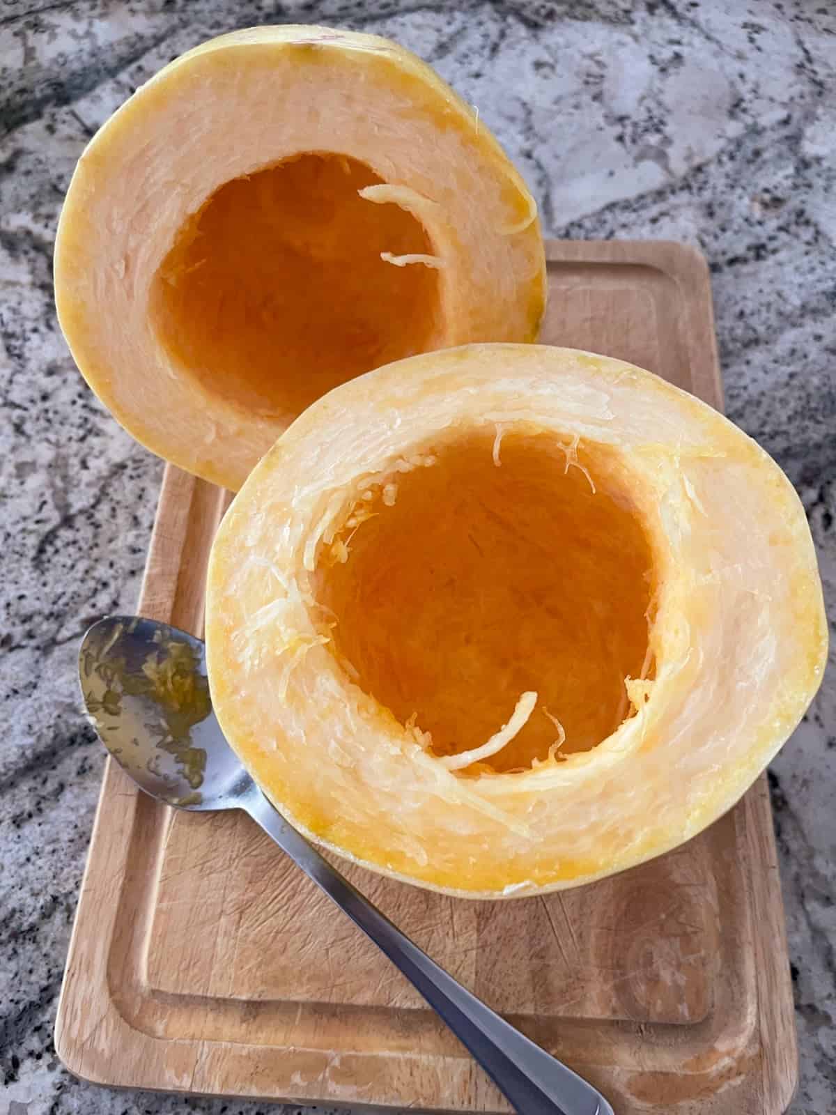 Spaghetti squash cut in half and cleaned of seeds on cutting board with spoon.