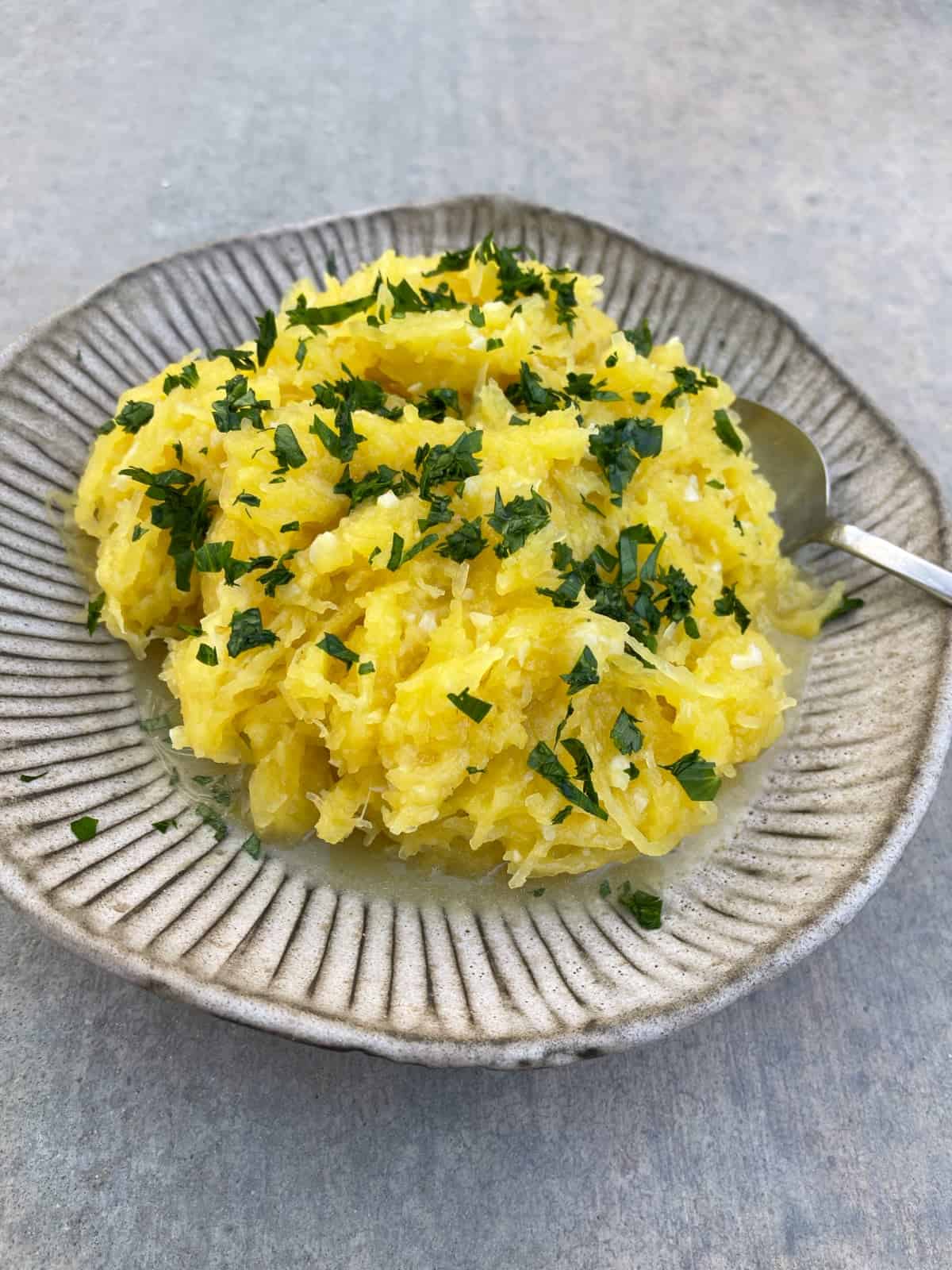 Instantpot Garlic Parmesan Spaghetti Squash topped with fresh parsley in ceramic serving bowl with spoon.