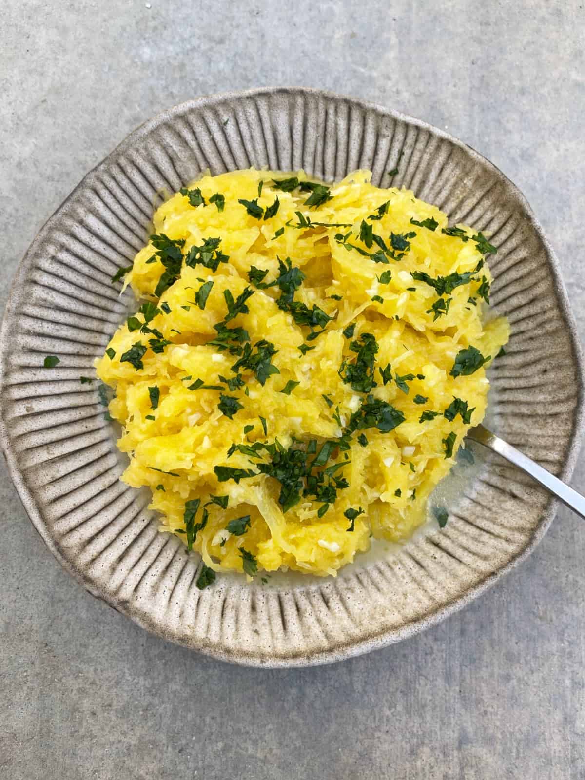 Instant pot garlic parmesan spaghetti squash garnished with chopped parsley in serving bowl with spoon.