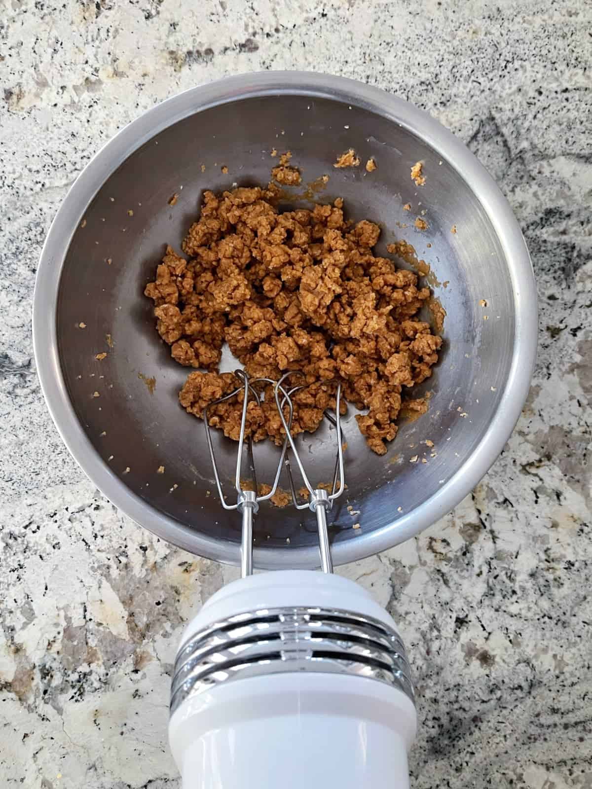Mixing peanut butter bon bon ingredients in bowl with electric hand mixer.
