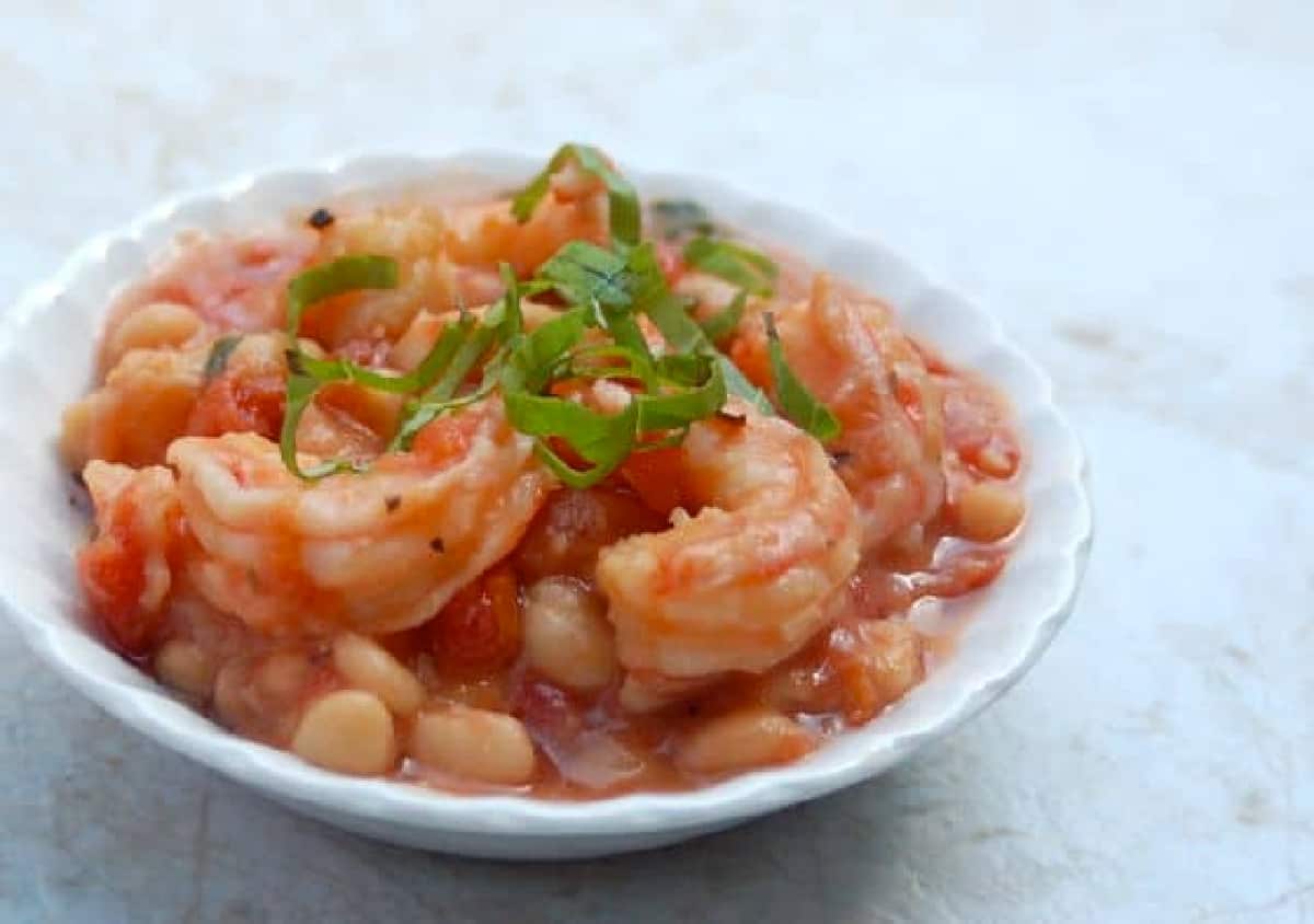 White China Bowl of Slow Cooker White Shrimp and Beans Garnished with Parsley on Granite Counter.