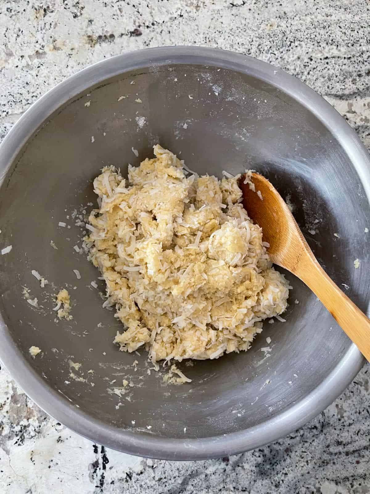 Stirring coconut macaroon kiss cookie dough with wooden spoon.