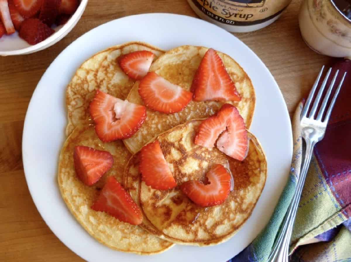 pancakes on a white plate topped with sliced strawberries with fork along right side.