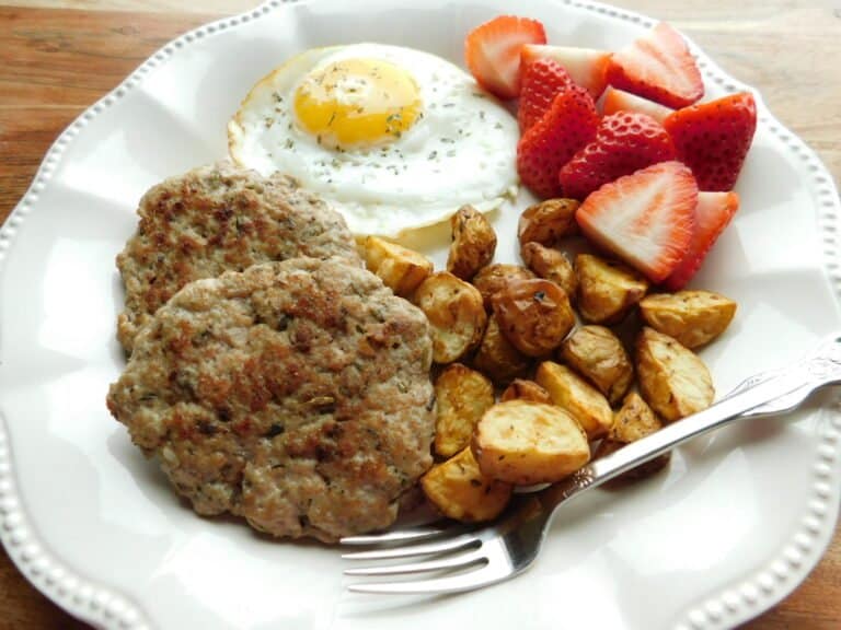 Turkey sausage patties, hash browns, sunny side up egg and sliced strawberries on white plate with fork in foreground.