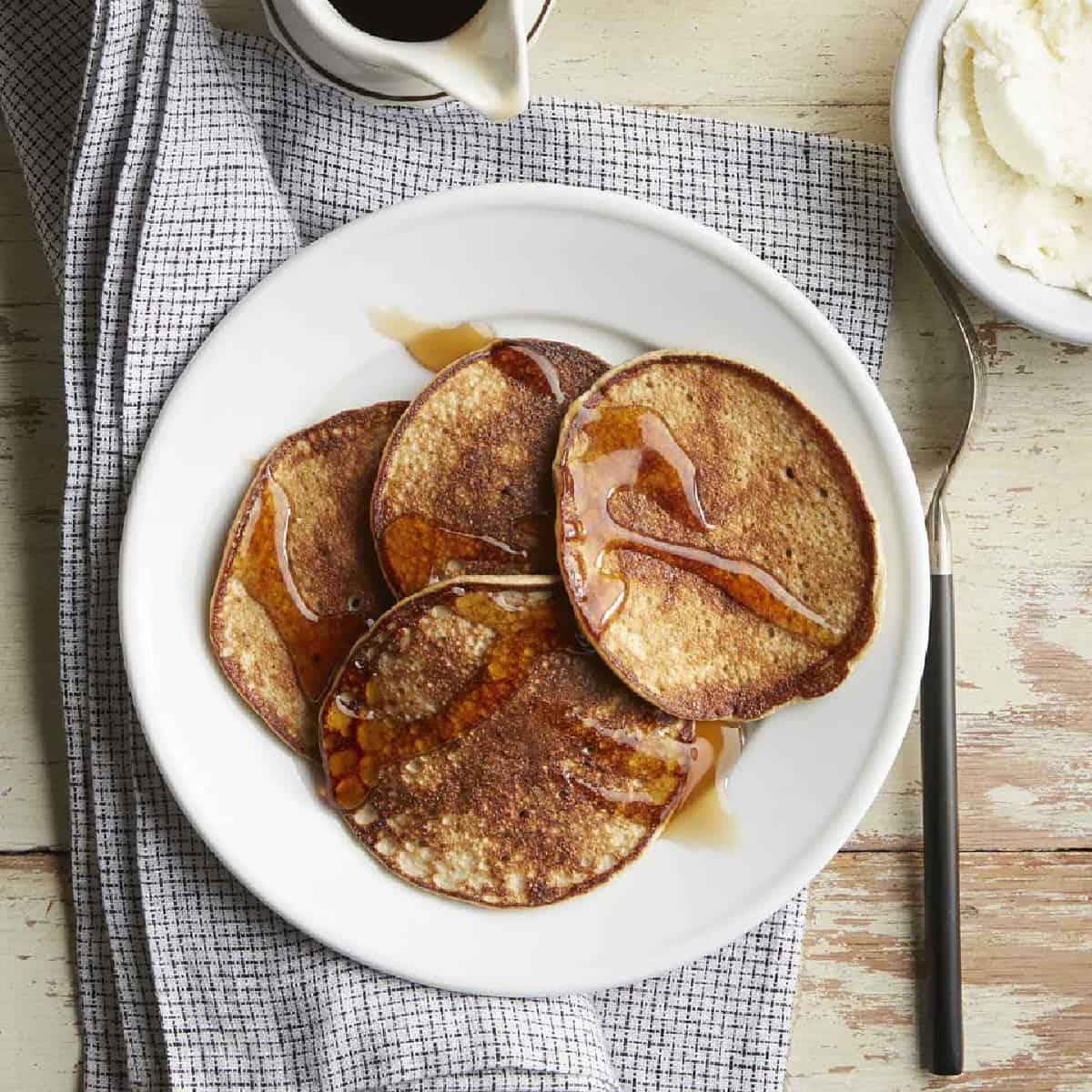 white plate with banana pancakes on gray towel from above