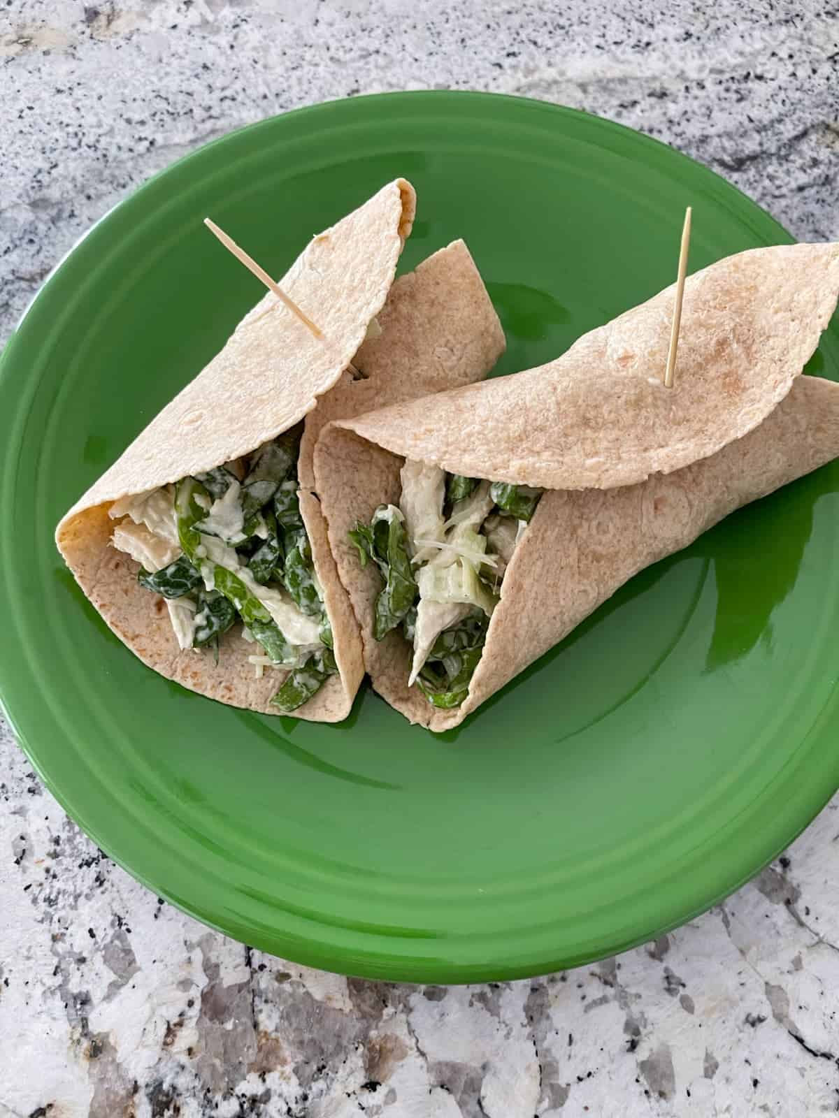 Two chicken Caesar salad wraps on large green plate.