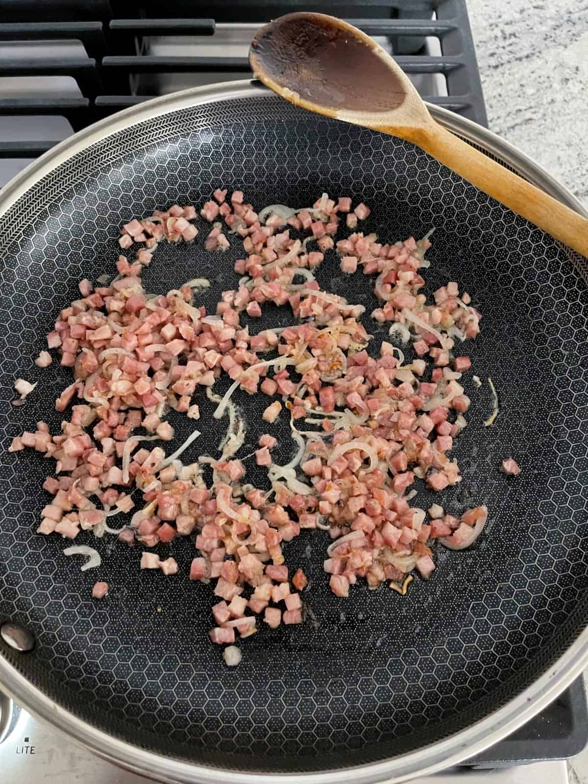 Sauteeing pancetta and shallots in skillet with wooden spoon.