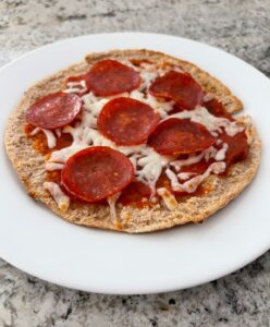 Pita bread topped with marinara sauce, mozzarella cheese and pepperoni on white plate