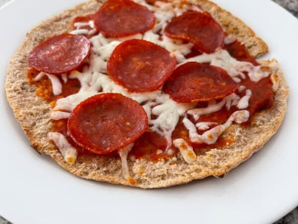Pita bread topped with marinara sauce, mozzarella cheese and pepperoni on white plate