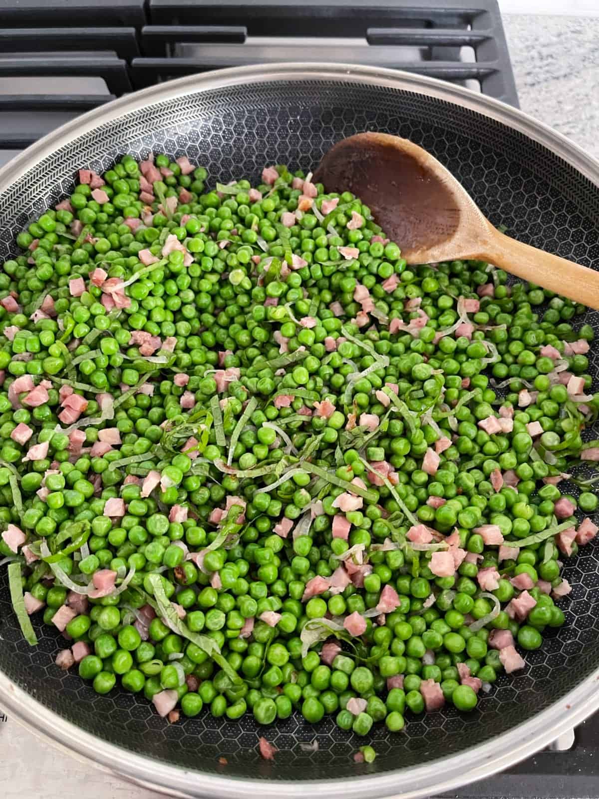 Cooking peas, pancetta and mint in skillet with wooden spoon.