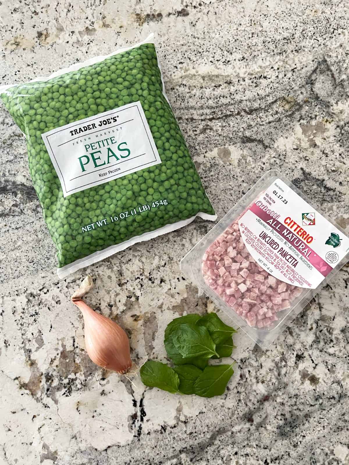 Bag of frozen peas, package of uncured pancetta, whole shallot and fresh mint leaves on granite.