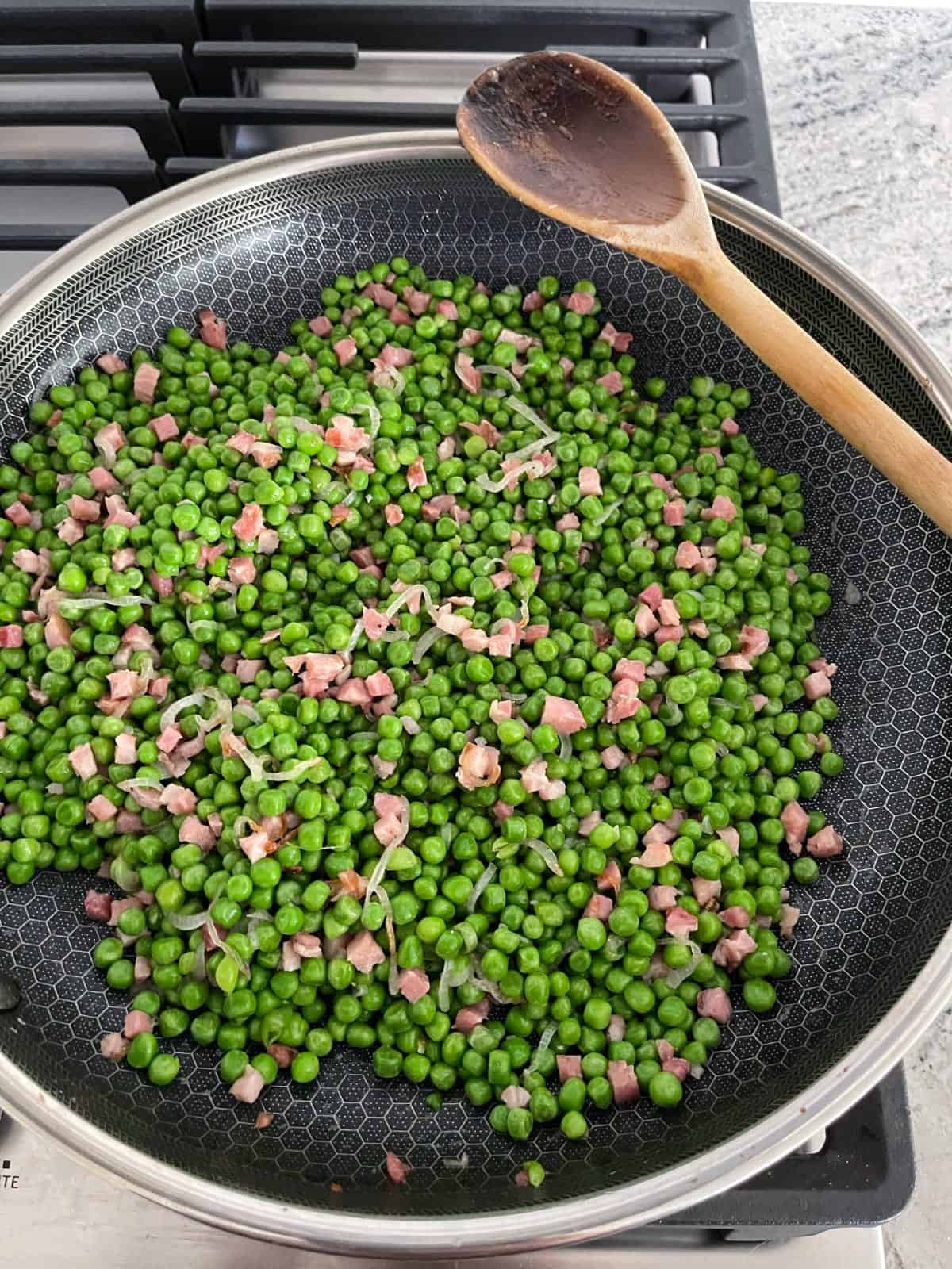 Cooking peas, pancetta and shallots in skillet with wooden spoon.