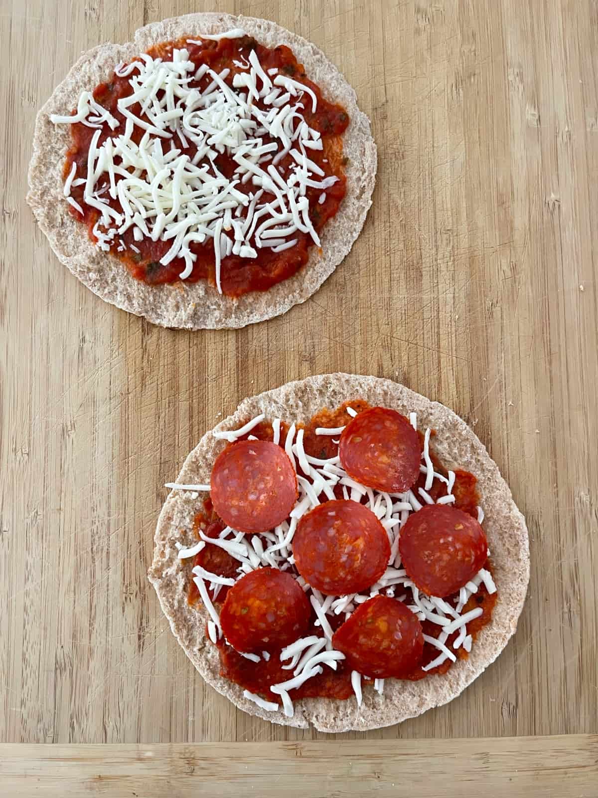 Two uncooked personal pita pizzas, one with just sauce and cheese and one with sauce, cheese and turkey pepperoni.
