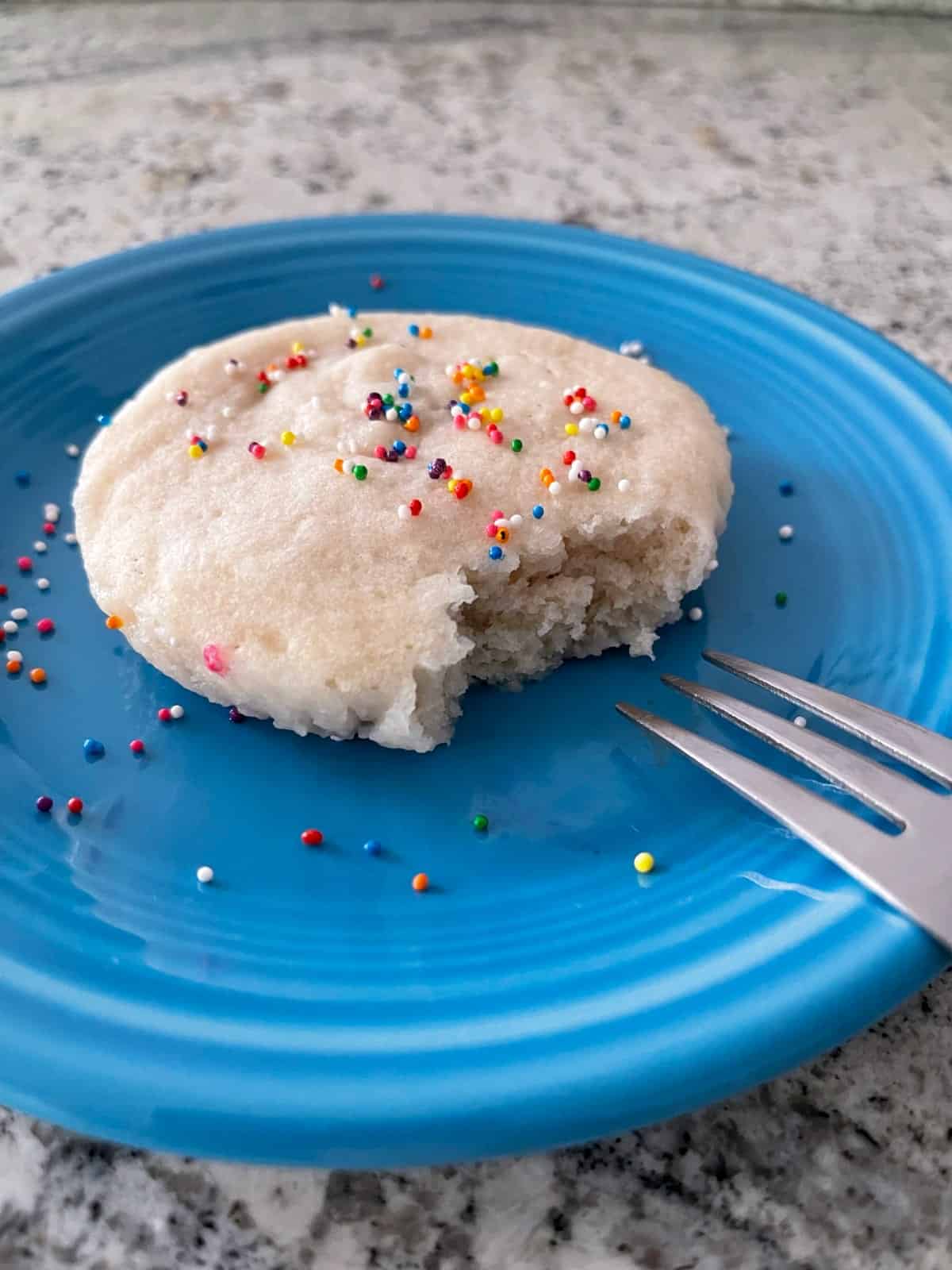 Microwave vanilla mug cake topped with rainbow sprinkles on small blue plate with fork.