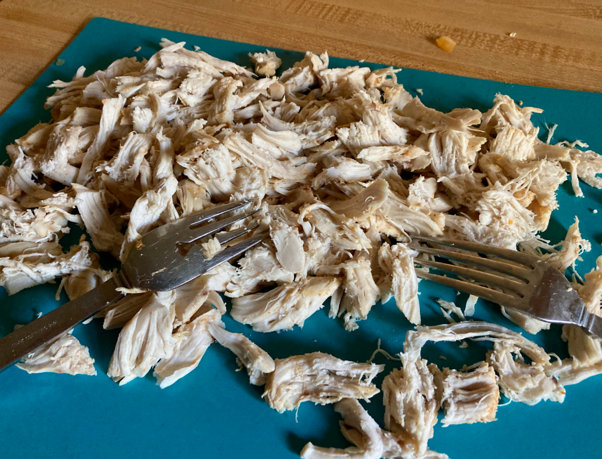 Pollo desmenuzado con dos tenedores en una tabla de cortar azul