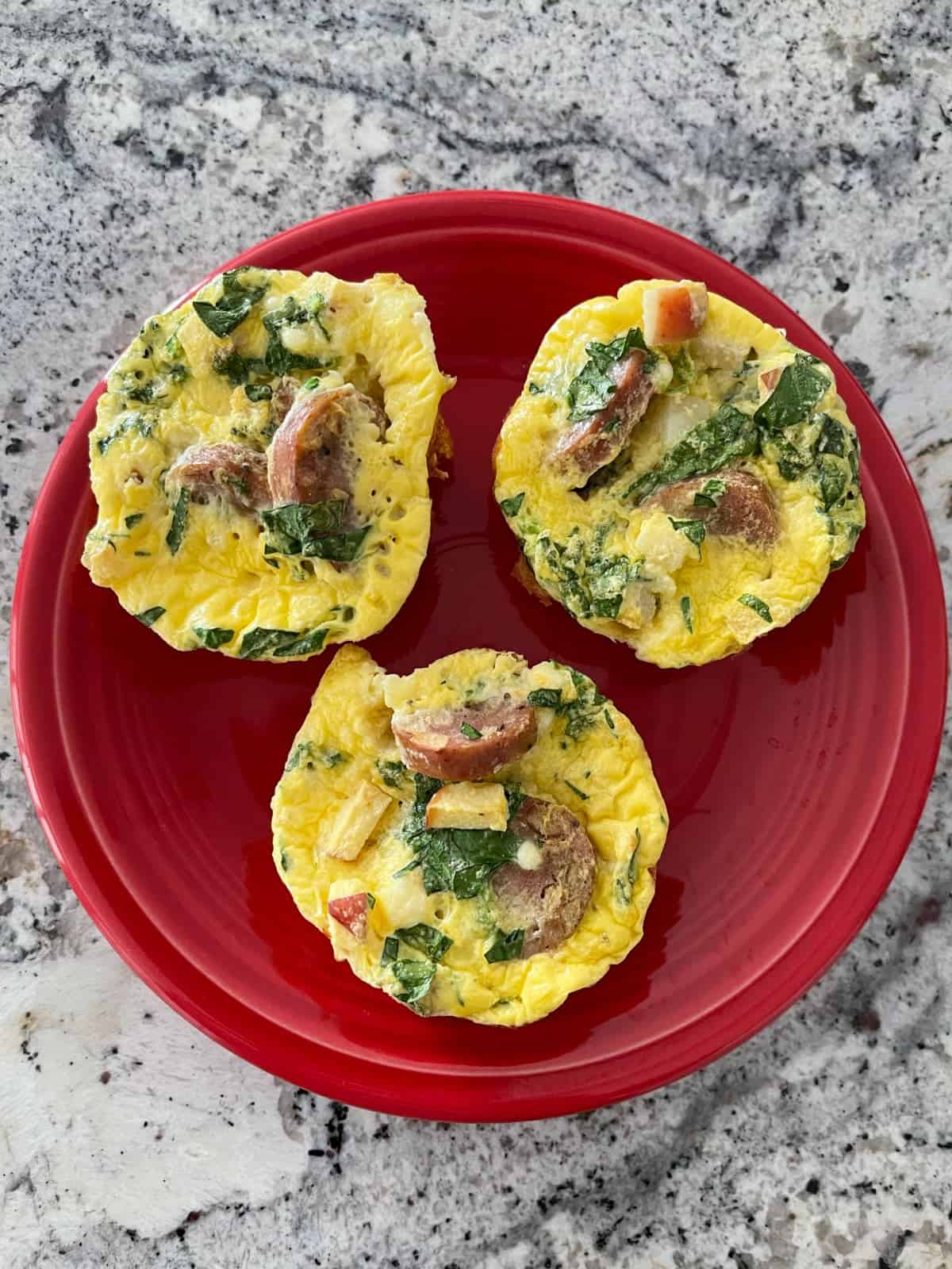 Fresh baked apple chicken sausage egg muffins on red plate.