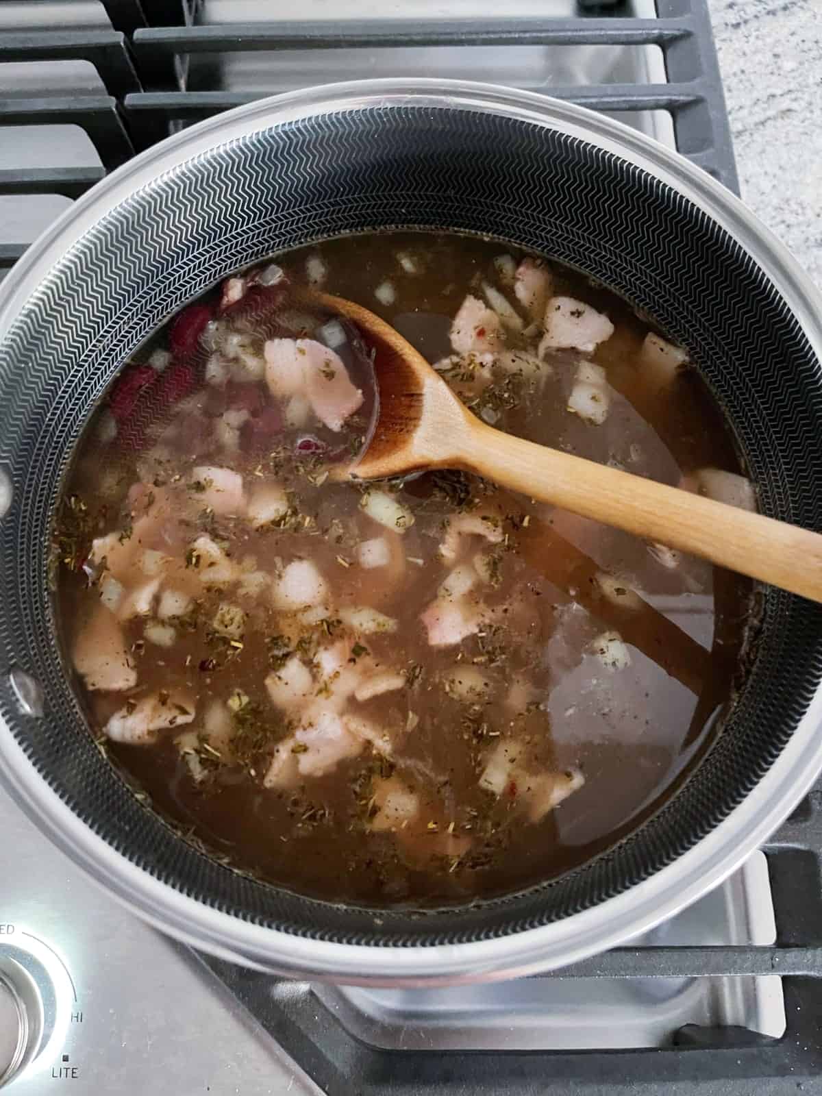 Cooking Jamaican Jerk red beans and rice soup in saucepan on stovetop.